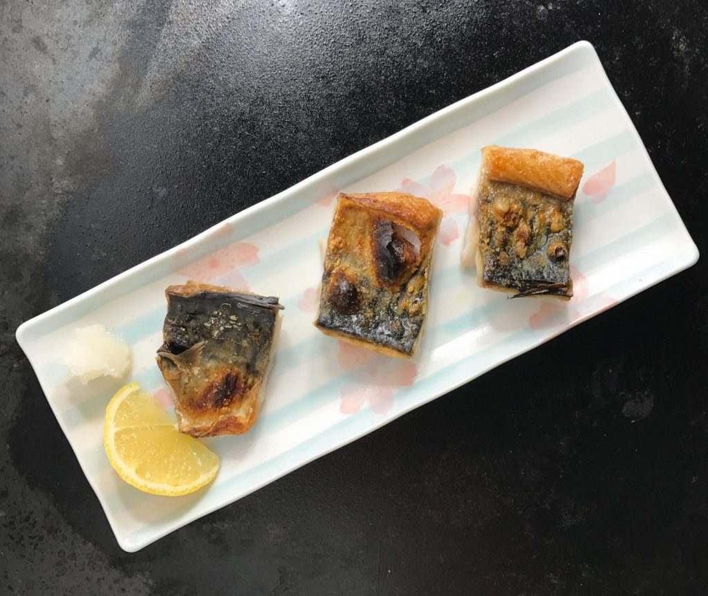 Presentation of sardines on a plate with lemon wedges.