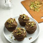 Four chocolate cupcakes with pistachios on a plate.