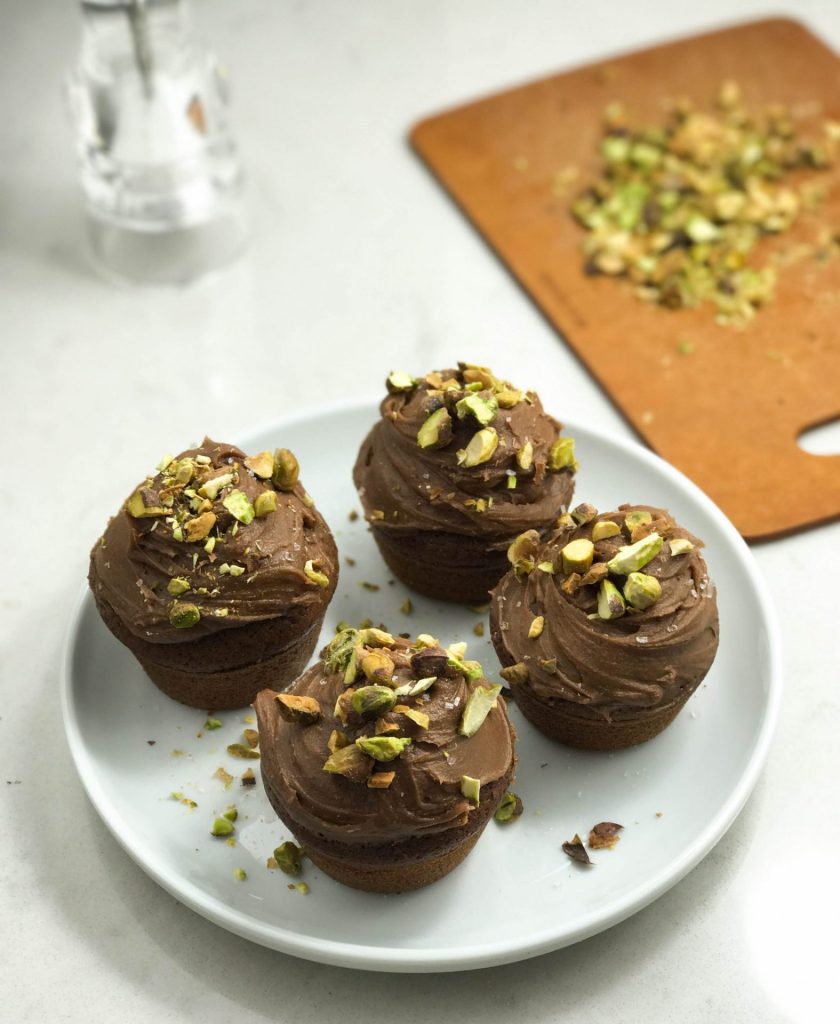 Four chocolate cupcakes with pistachios on a plate.