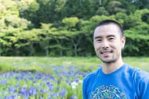 A man in a blue shirt surrounded by purple flowers.