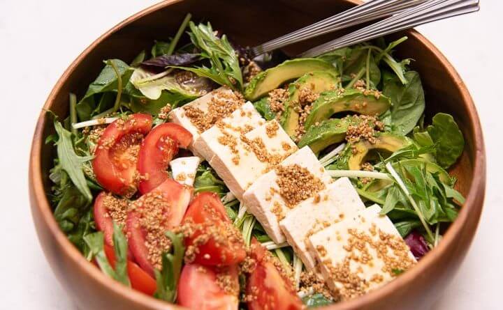 A Japanese vegetarian dish featuring a bowl of salad with tofu, tomatoes and avocado.