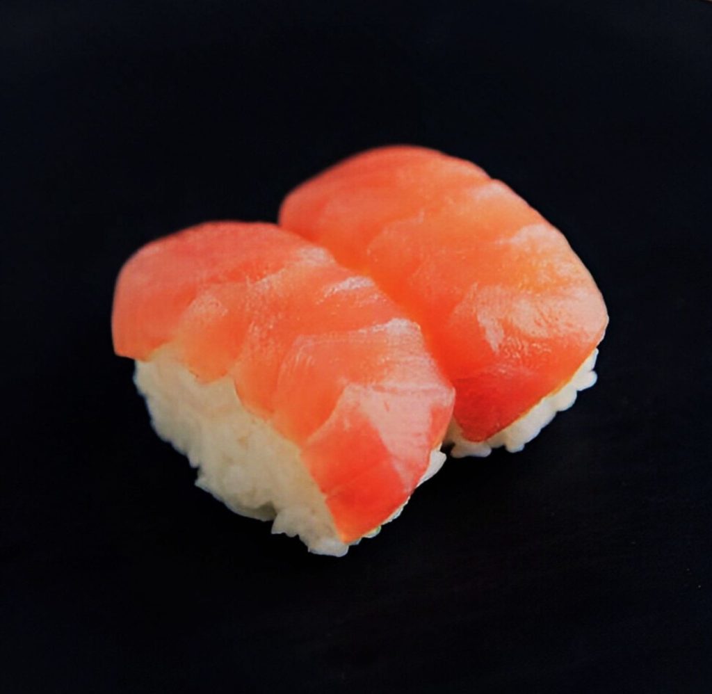 Sushi grade salmon sushi on a black surface.