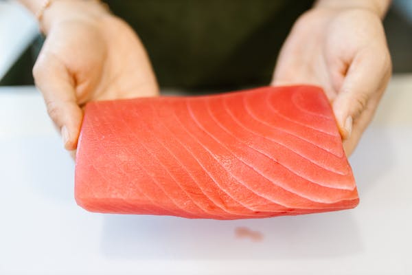 A person holding a piece of sushi grade salmon in their hands.