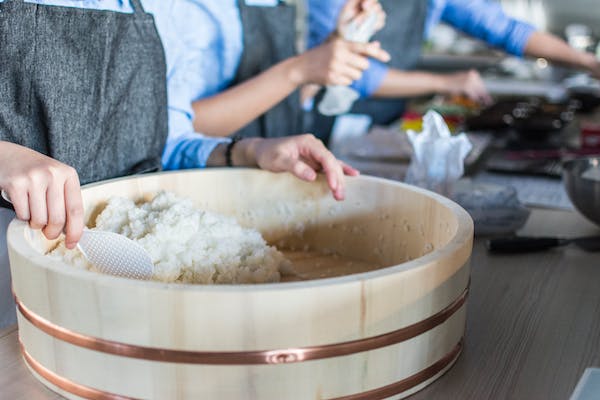 A group of people preparing sushi in a wooden bowl.