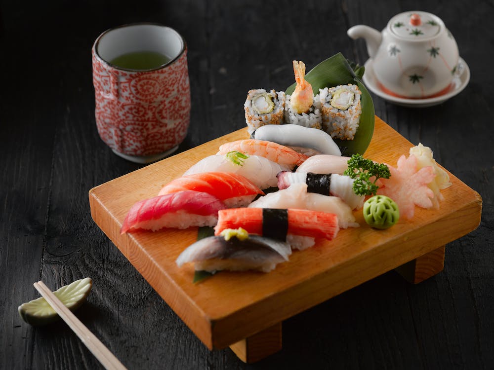 Traditional Japanese sushi beautifully presented on a wooden board accompanied by a soothing cup of tea that perfectly complements the delicate flavors.