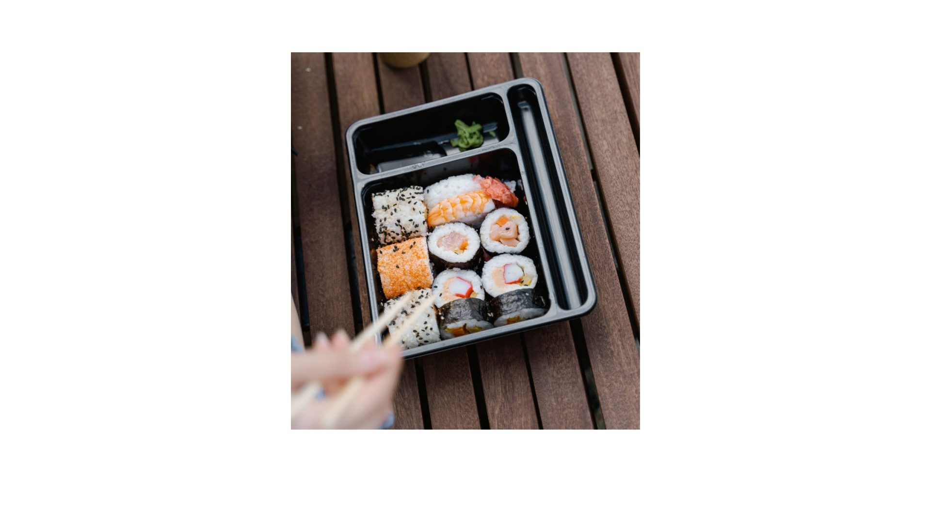 A person is holding sushi in a plastic container.