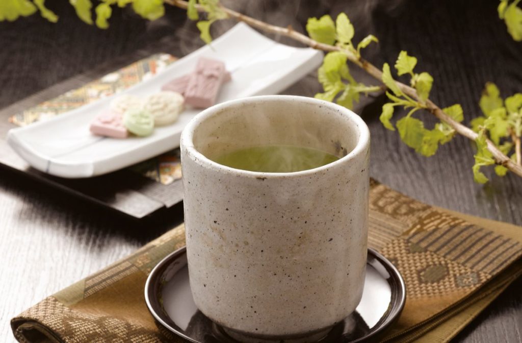 hot green tea in cup with wagashi in background