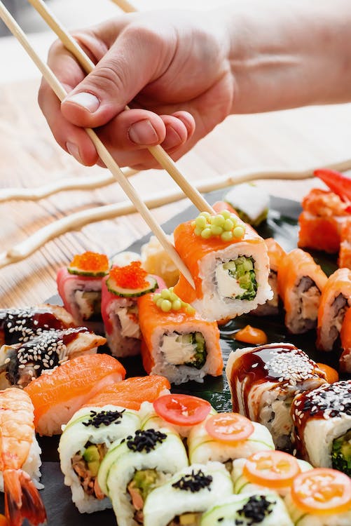 A person holding chopsticks over a plate of sushi.