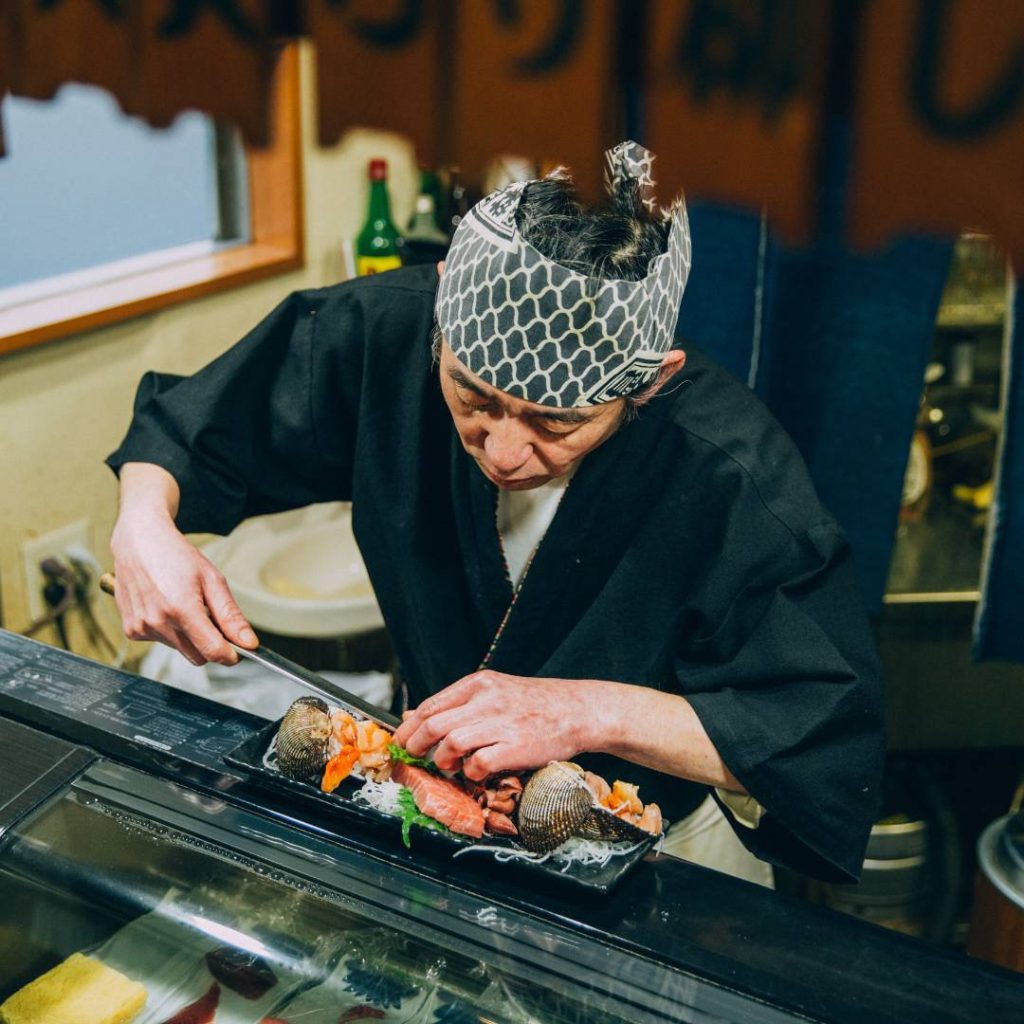 A man is preparing sushi containing carbs in a restaurant.