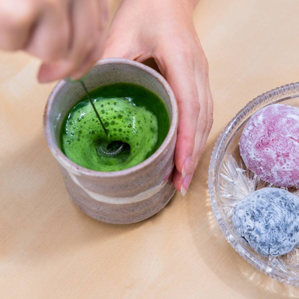 A person is using an electric whisk to froth green tea.