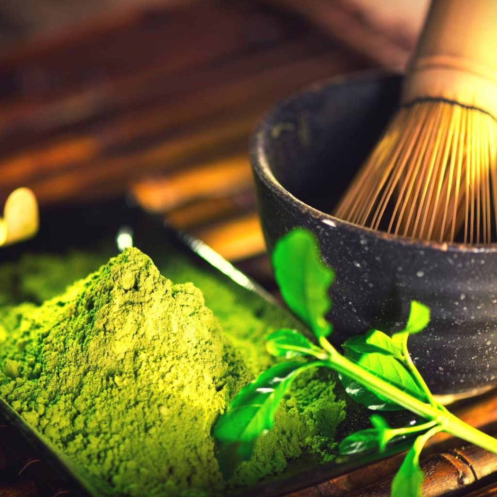 Matcha powder in a bowl with a bamboo whisk, creating a traditional matcha beverage.