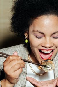 A woman delicately using chopsticks to enjoy sushi with roe.