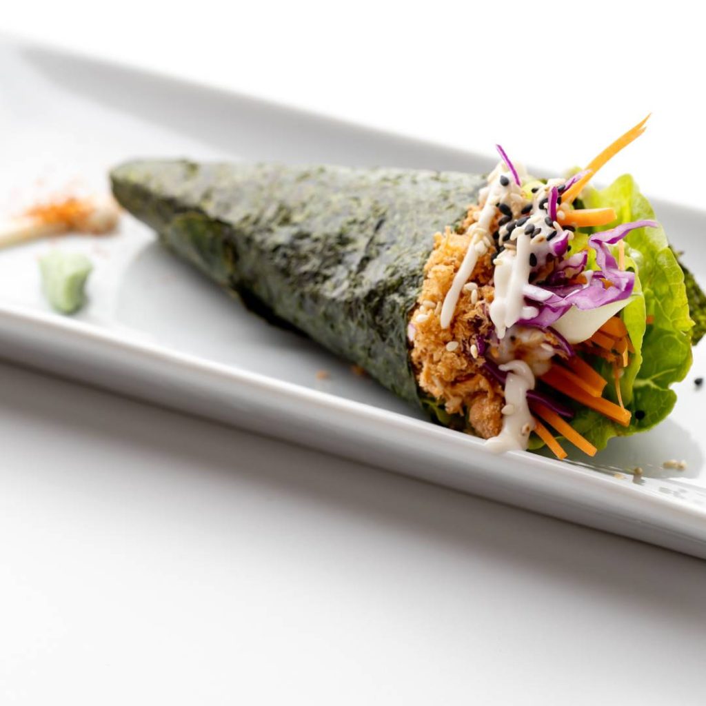 A handroll is sitting on a white plate.