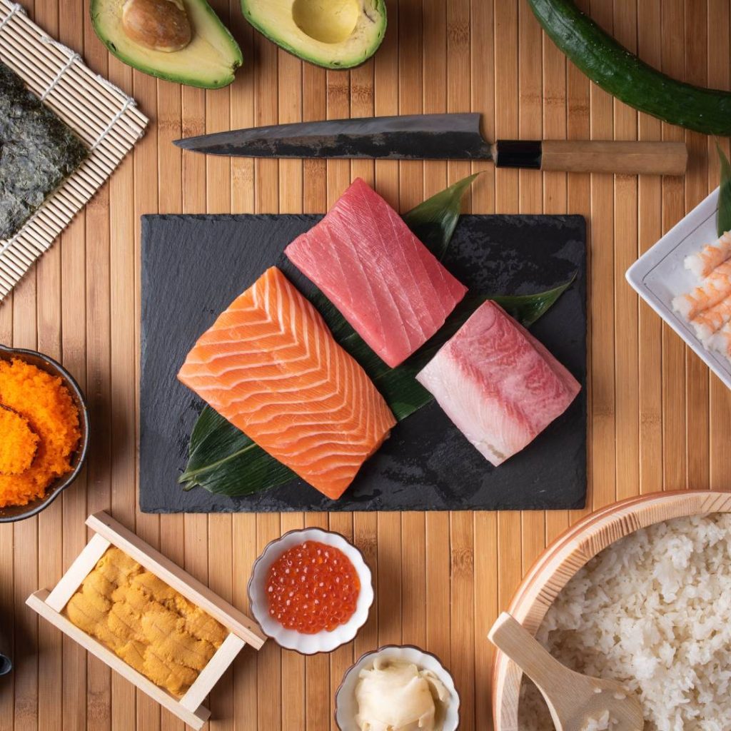 Handroll sushi and vegetables displayed on a wooden table.