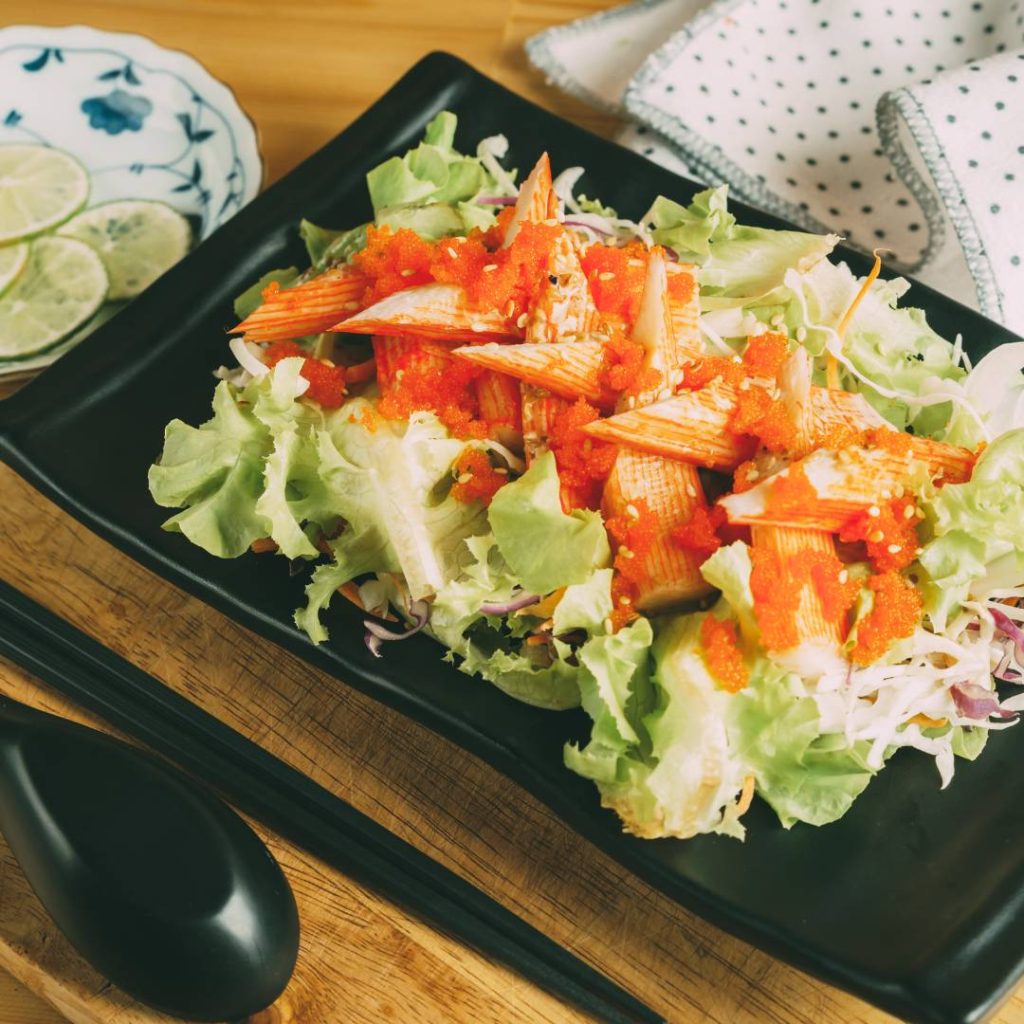 A black plate with a kani salad on it.