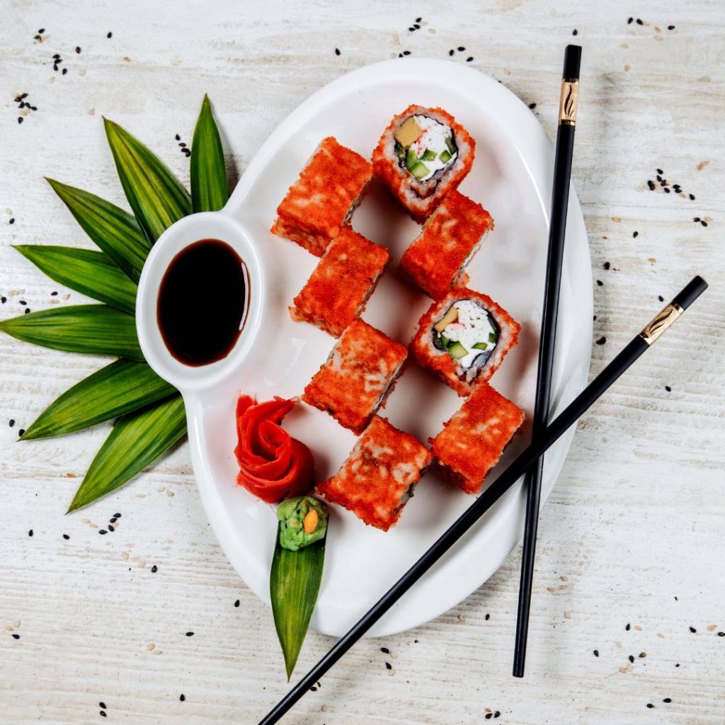 Kani sushi on a plate with chopsticks and sauce.