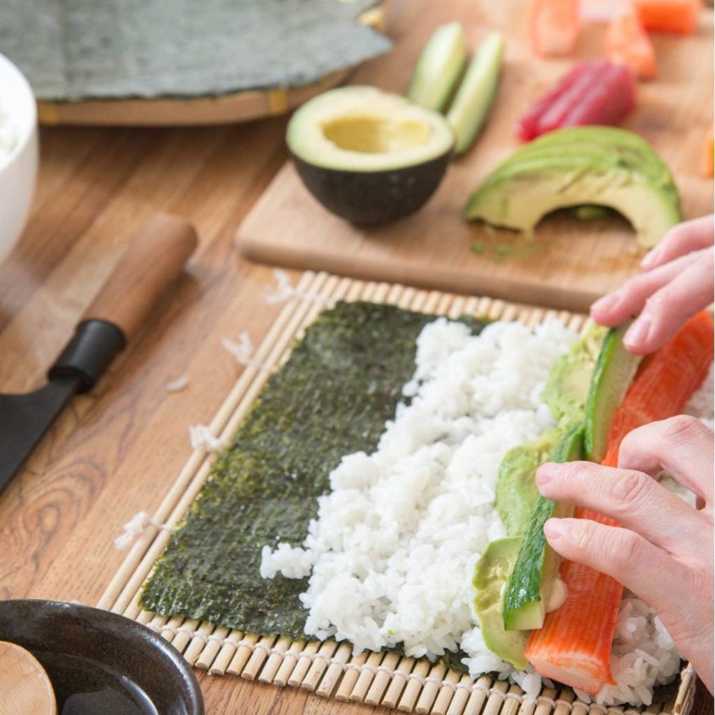 A person handrolling sushi on a wooden cutting board.