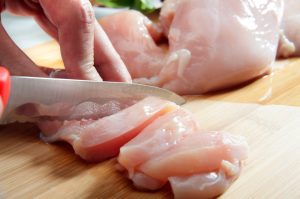 A person cutting chicken with a knife on safest cutting board for chicken.