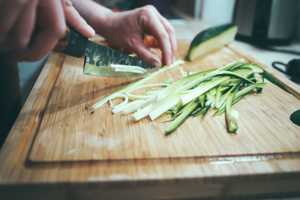 A person preparing zucchini on a wooden cutting board.