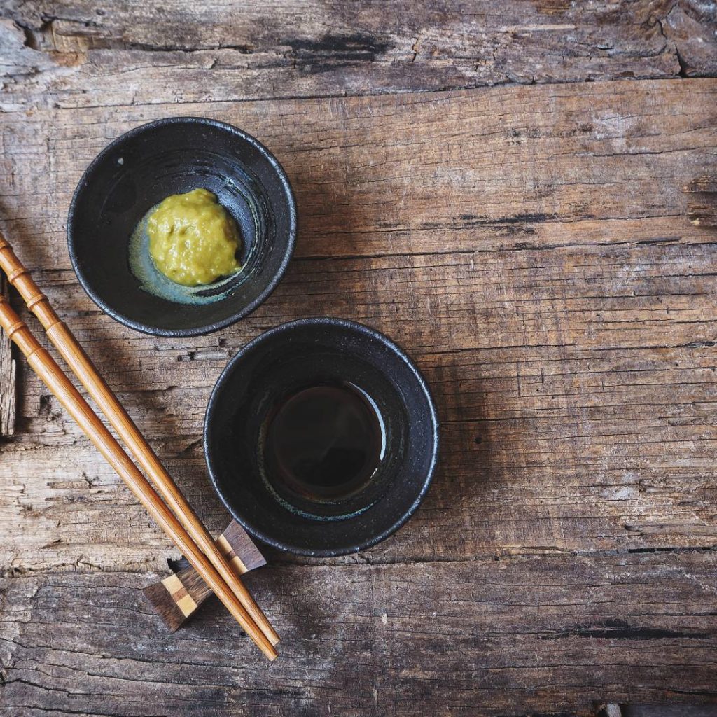 Two sushi bowls with soy sauce and wasabi on a wooden table.