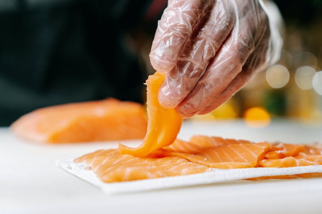 A person is slicing salmon for sushi on a cutting board.