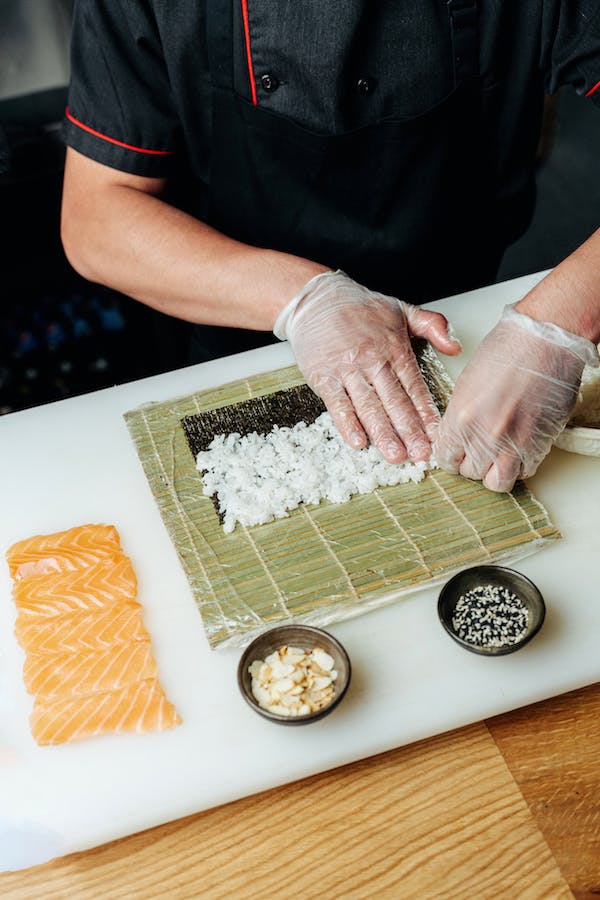 A sushi chef is expertly preparing delectable sushi on a cutting board with impeccable taste.