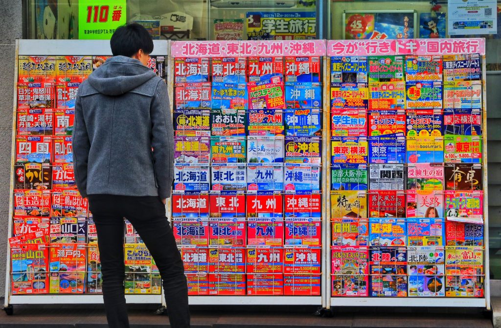 A man standing in front of a display of Okinawa magazines.