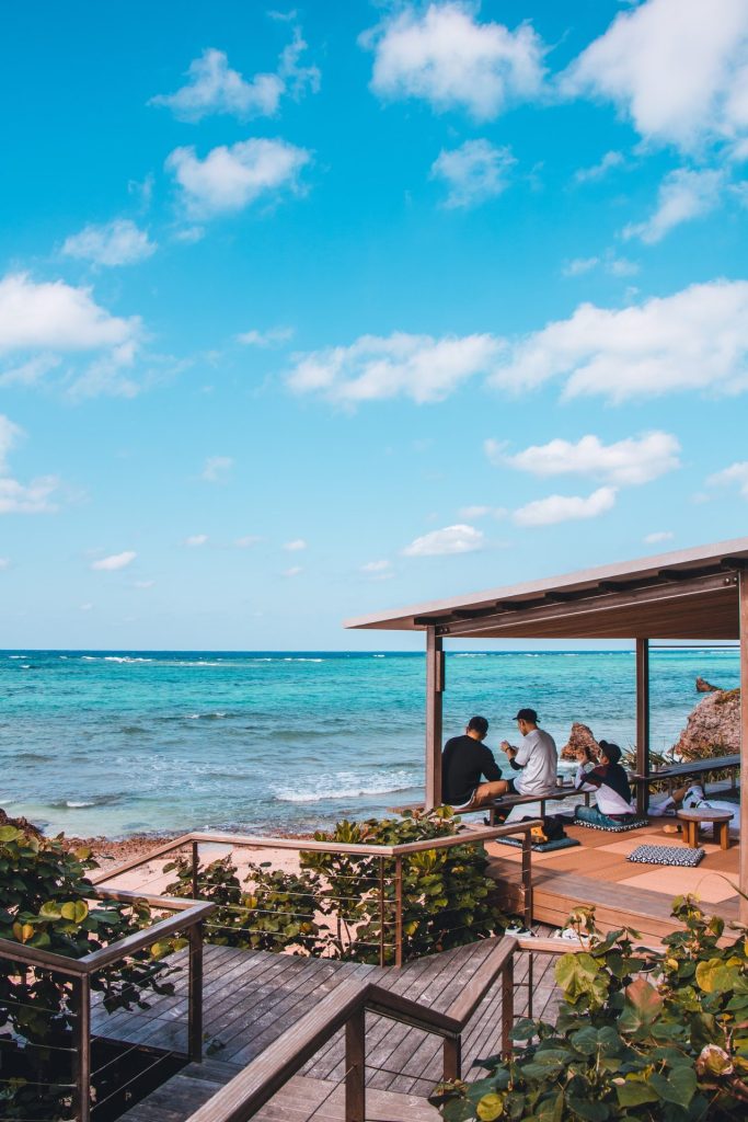 A group of people sitting on a wooden deck overlooking the ocean in Okinawa.