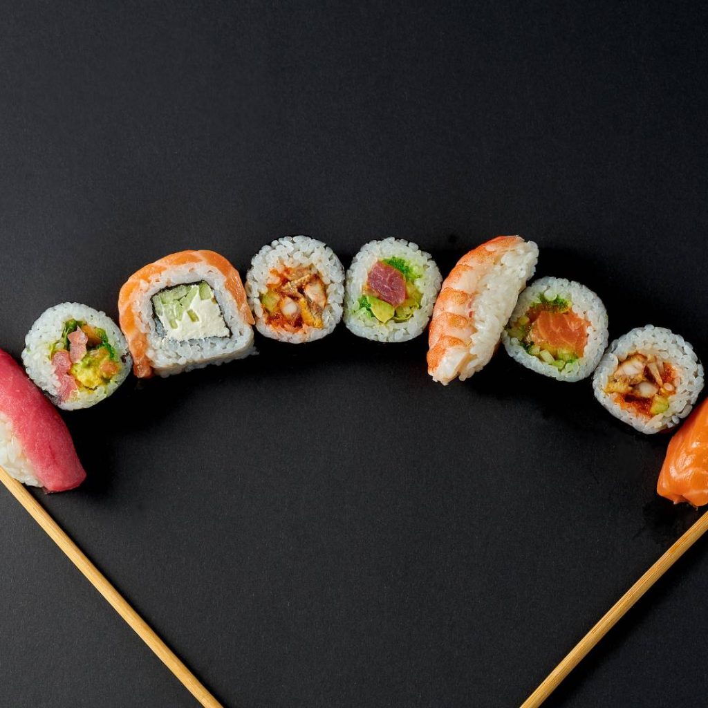 Sushi rolls on a black background with chopsticks.