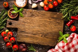 A wooden cutting board with tomatoes, herbs and spices on a wooden background.