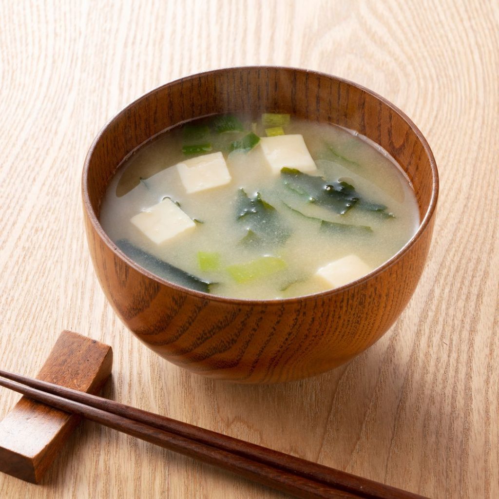 A bowl of Japanese tofu miso soup sits on the table with a pair of chopsticks.