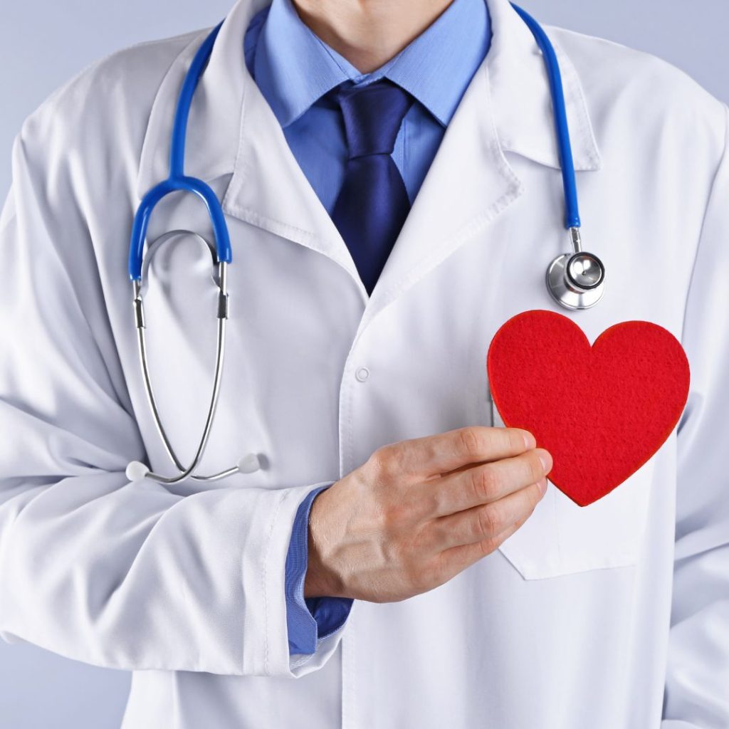 A doctor raises a cut-out heart to his chest.