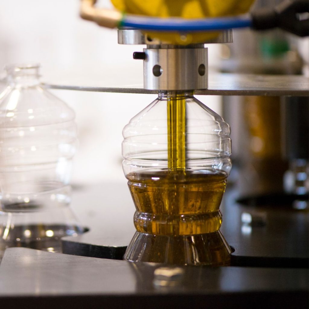 A factory machine transfers olive oil to a plastic bottle.