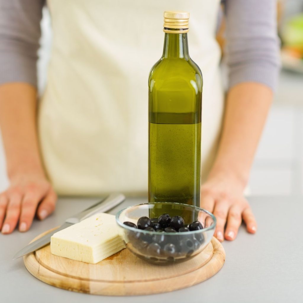 A woman stands in front of an extra virgin olive oil bottle.