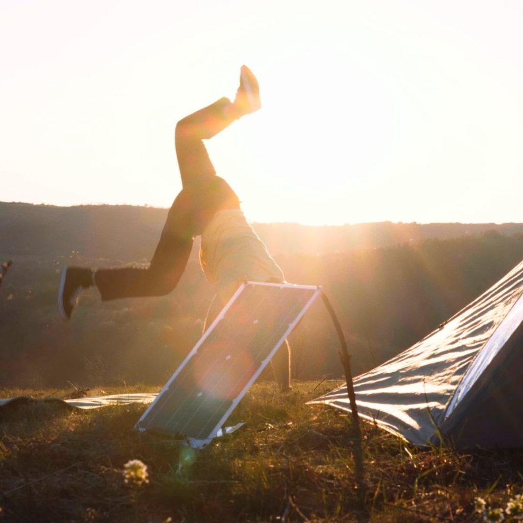 A person performing a handstand using the Jackery SolarSaga 200W Solar Panel in front of a tent.