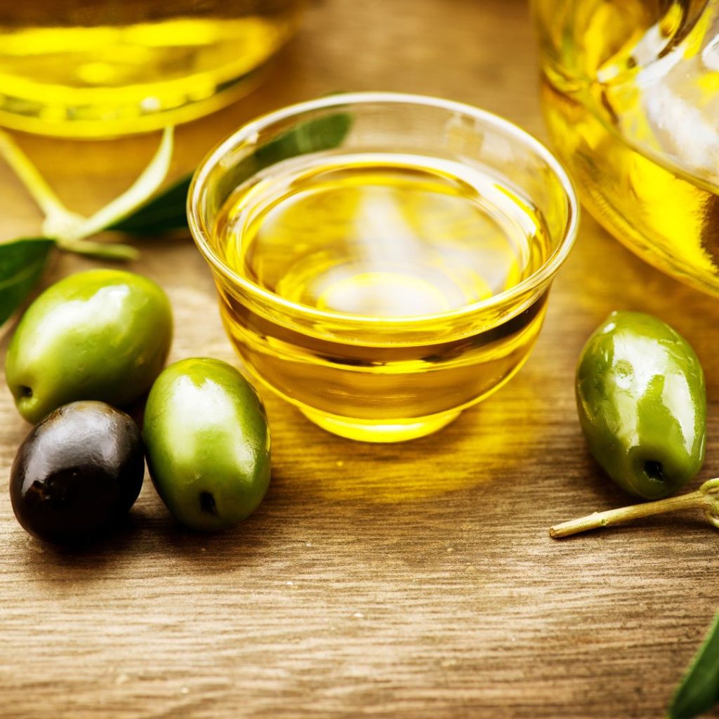 Extra virgin olive oil sits on a table with olives.