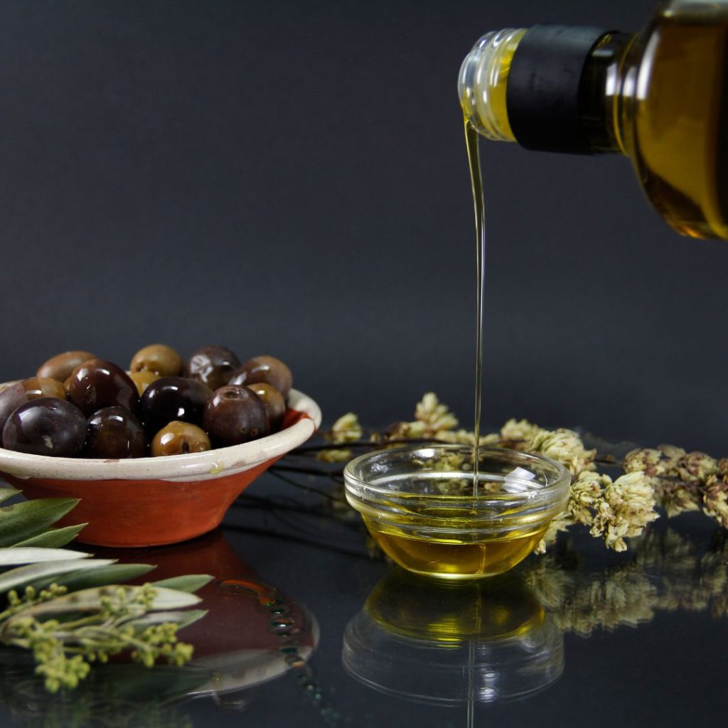 Extra virgin olive oil gets poured into a small container beside fresh olives.