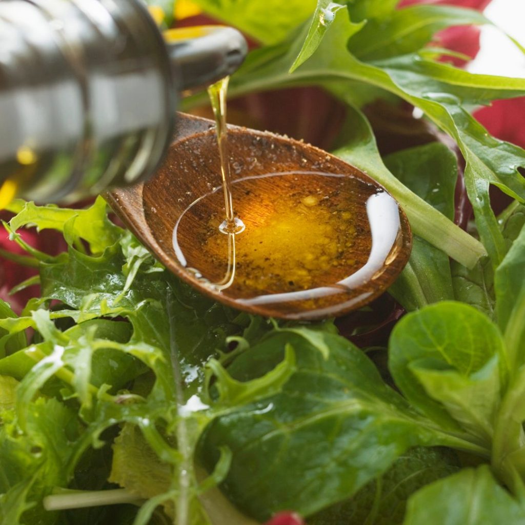 Extra virgin olive oil gets poured on a wooden spoon before drizzling it into a salad bowl.