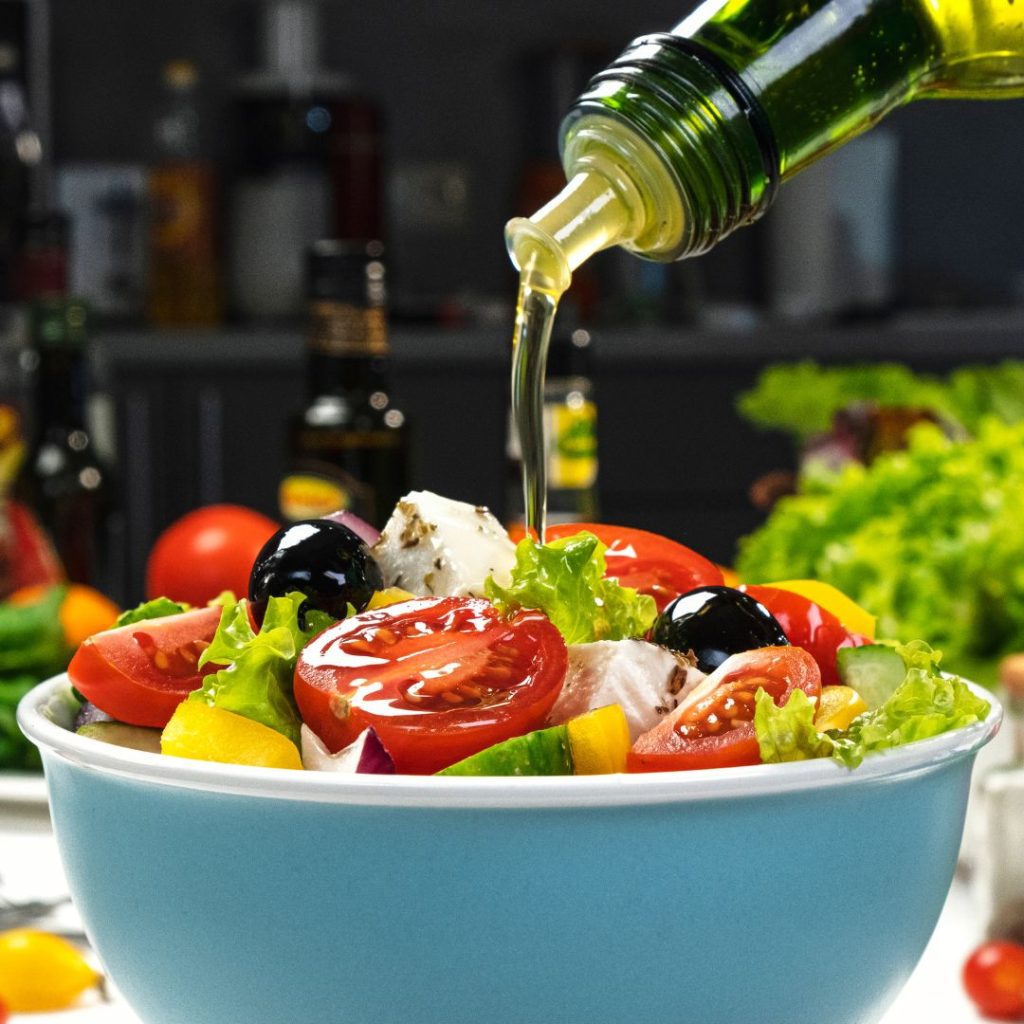 Extra virgin olive oil being poured into a bowl of salad.