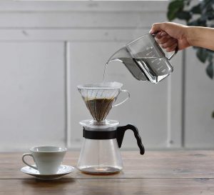 A person reviewing the Hario Air Kettle while pouring coffee into a cup on a table.