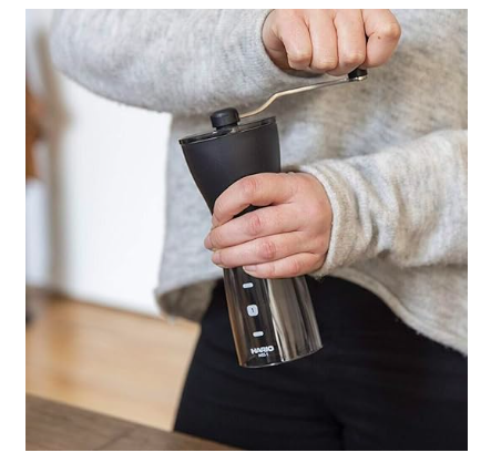 A person using the Hario Mini-Slim Plus coffee grinder on a table.