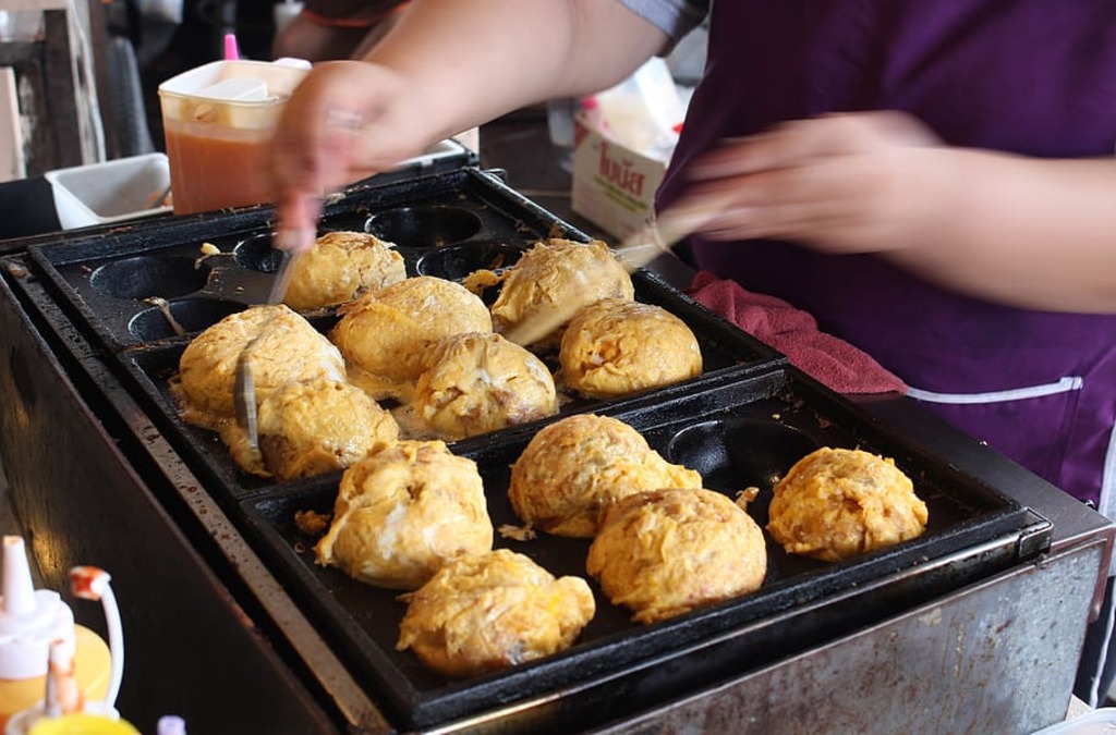 A person is reheating some takoyaki in a pan.