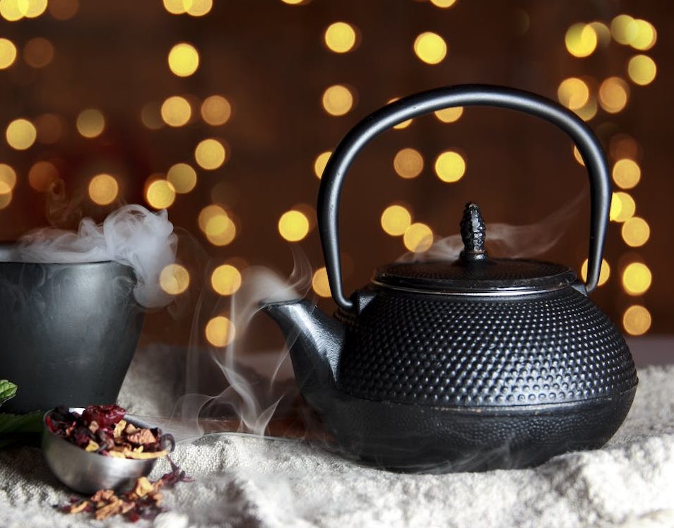 A cast iron Japanese teapot next to a cup of tea on a table.