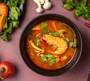 A bowl of Thai prawn soup, keto-friendly, on a red background.