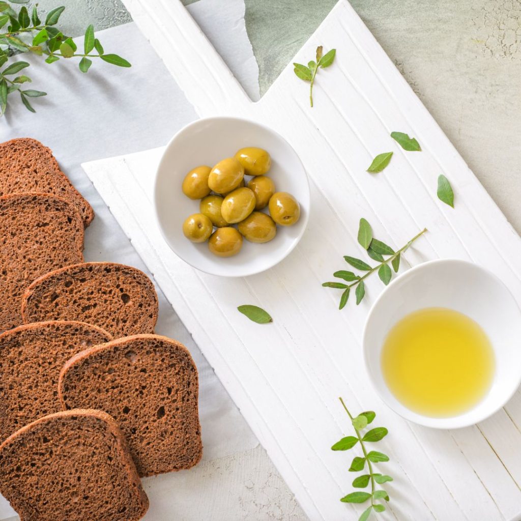 Loaves of bread, a bowl of olives, and a bowl of olive oil lays down on the table.