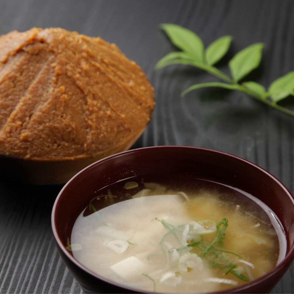 A bowl Miso Soup with a miso paste next to it.