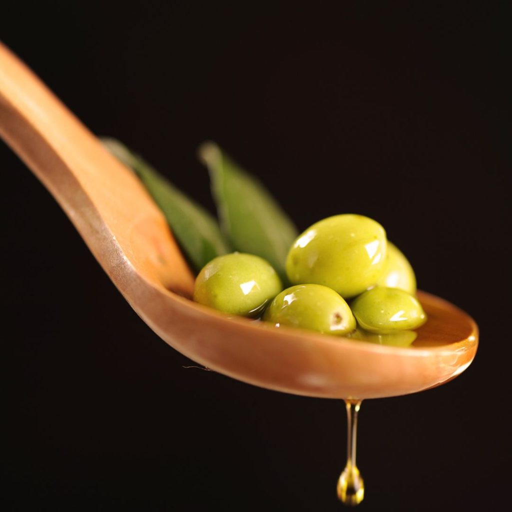 Olive oil drips from a spoonful of olives