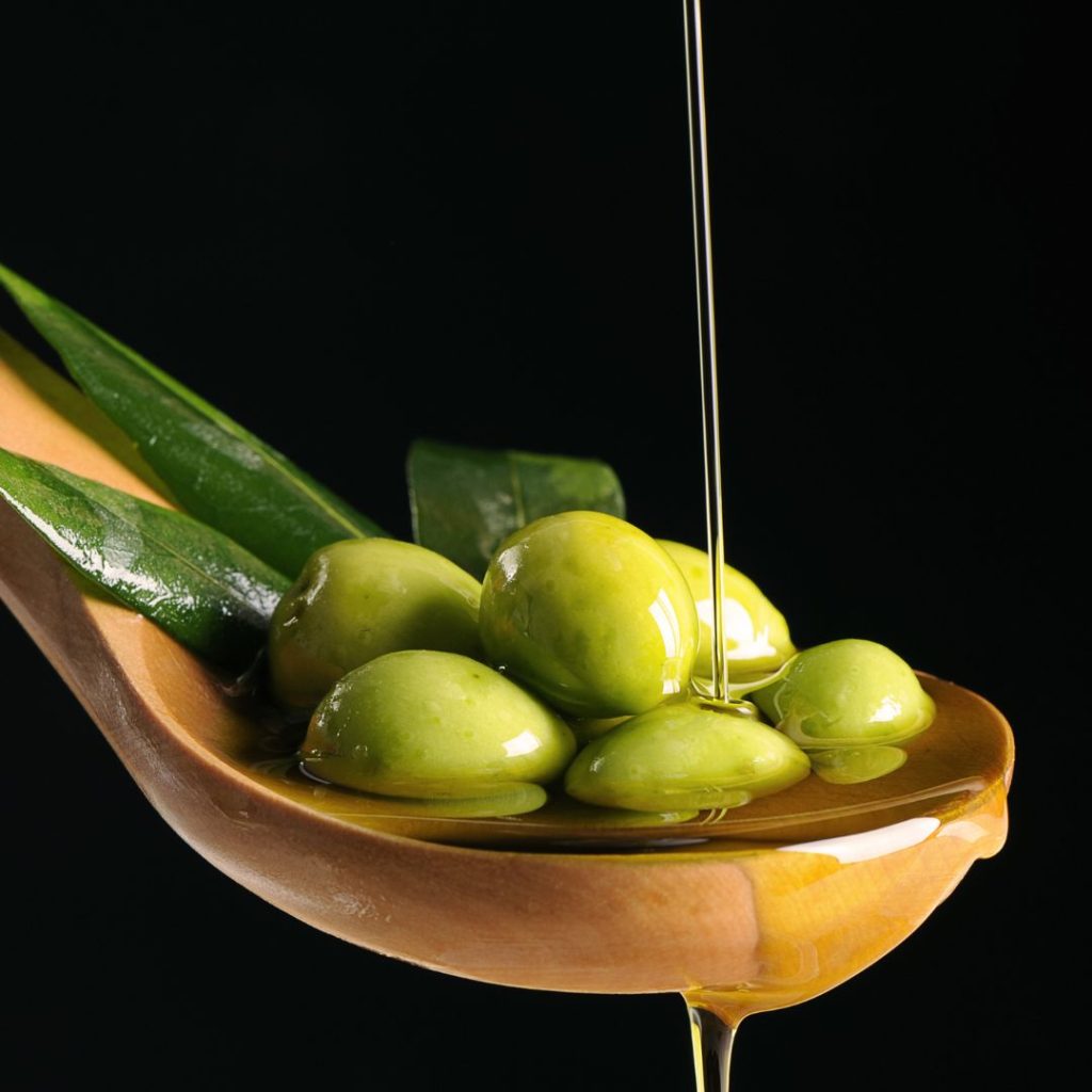 Olive oil drips from a wooden spoon full of olives.