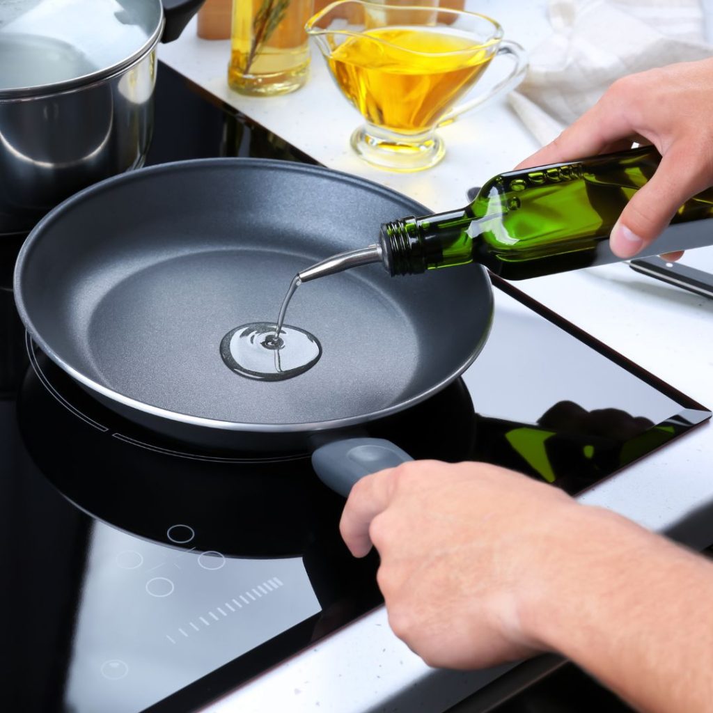 A person pouring olive oil into a frying pan.