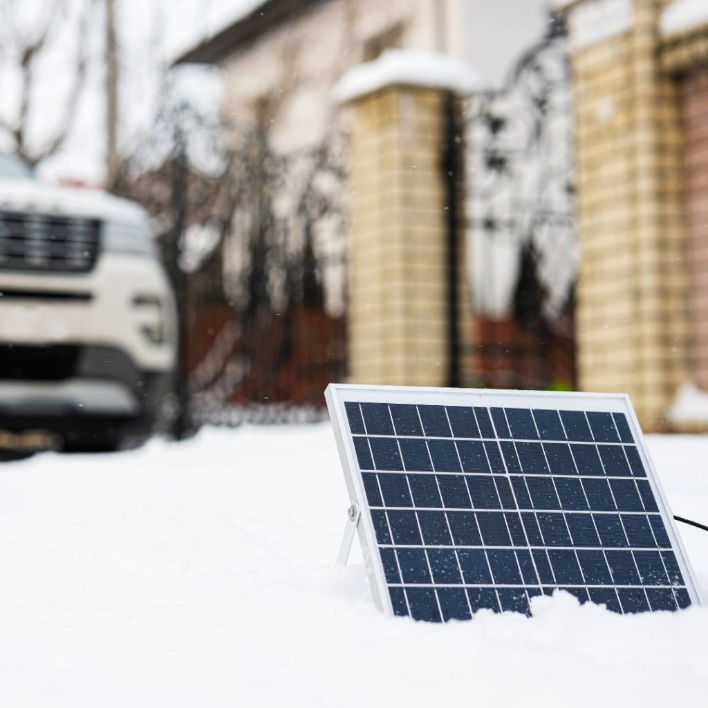 A solar panel adjacent to a car covered in snow.